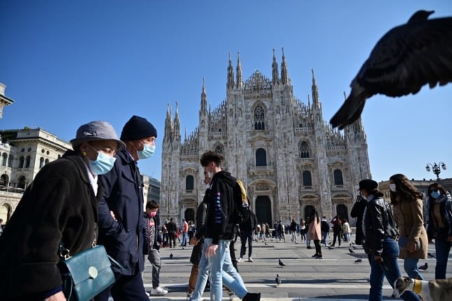 People walk in central Milan wearing face masks.