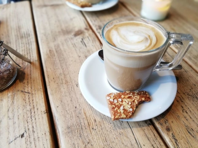 A foamy caffe latte with a biscuit.