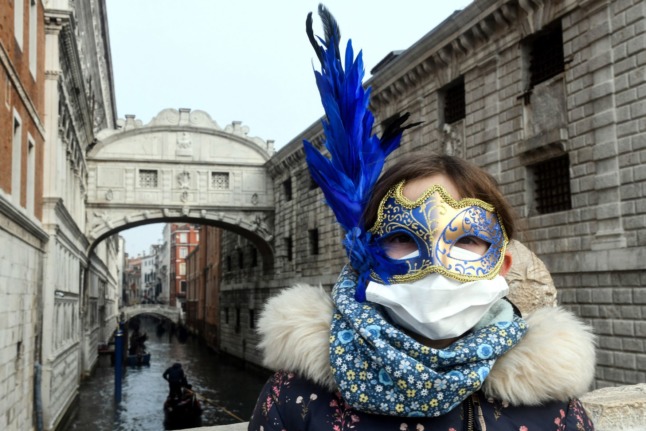A tourist wears a protective facemask and a Carnival mask in Venice on February 24, 2020, when Carnival festivities would normally be occurring. 