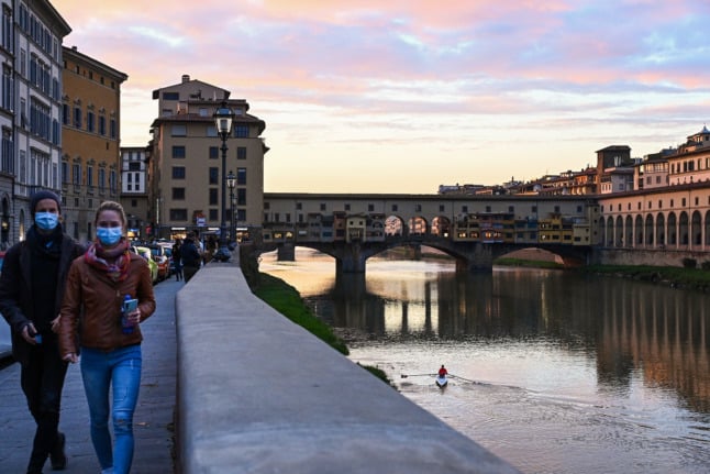 People walk at twilight along the Arno river near the Ponte Vecchio in downtown Florence, Tuscany.