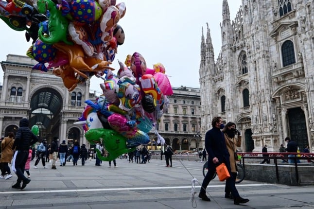 A couple wearing protective masks walk past balloons in front of the Duomo of Milan on January 3, 2022. - The use of FP2 masks in transport, stadiums, movie theatres, museums and sporting events is now mandatory in Italy. Wearing a mask outdoor is already mandatory since December 23rd.